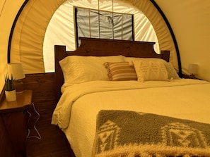 A tent-style room with a bed, pillows, a bedside lamp, and a blanket.