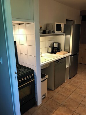 Una cocina compacta con estufa, microondas, refrigerador y cafetera sobre la encimera.