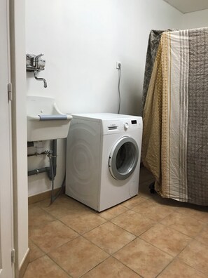 Un lavadero pequeño con lavadora, lavamanos y cortina de ducha.