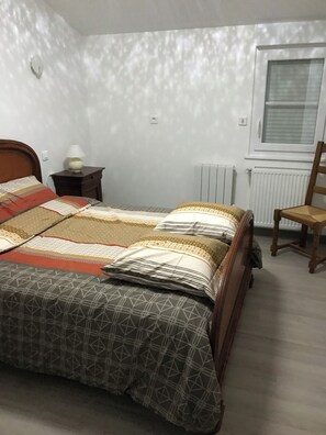 Un dormitorio con cama, mesita de noche con lámpara, radiador y ventana.