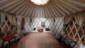 A yurt with a bed, wooden lattice walls, and a circular skylight.