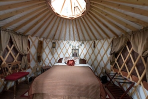 A yurt with a bed, wooden lattice walls, and a circular skylight.