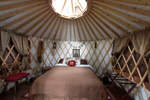 A yurt with a bed, wooden lattice walls, and a circular skylight.