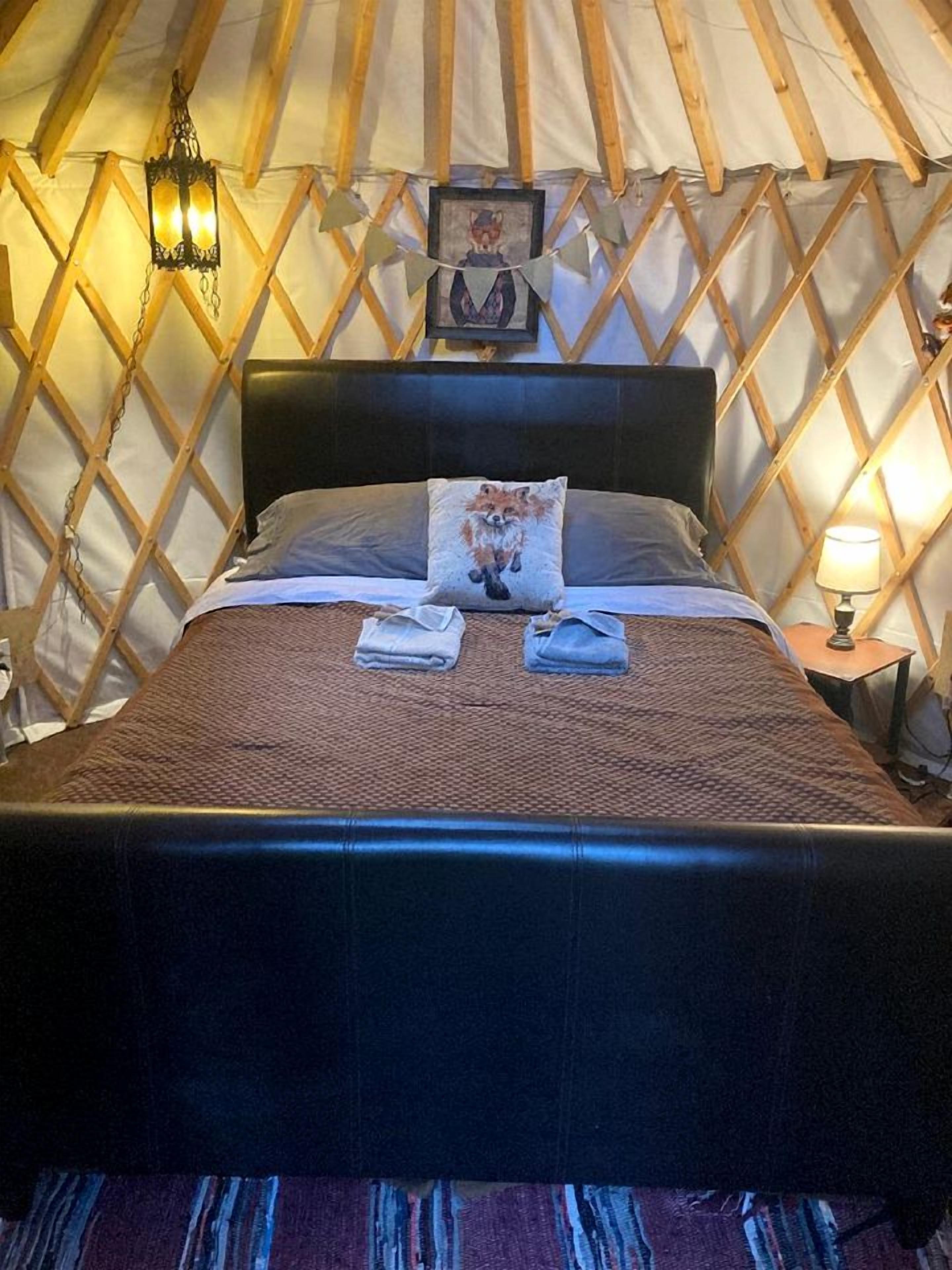 Ein Bett mit Kopfteil, ein Kissen mit Fuchs-Motiv, eine Decke und ein hängender Laternenleuchter.