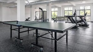 A gym with a ping pong table, exercise equipment, and large windows.