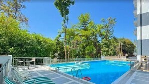 A swimming pool with lounge chairs, surrounded by trees and a tiled deck.