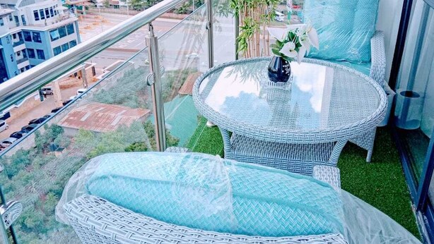 A balcony with wicker furniture, a glass table, and a view of a cityscape.