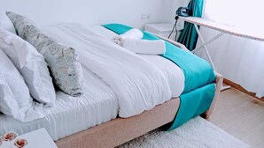 A neatly made bed with white and teal bedding, a small bedside table, and a teal curtain.