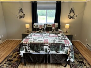 Un dormitorio con una cama grande, dos mesitas de noche, una ventana con cortinas y un aplique de pared.