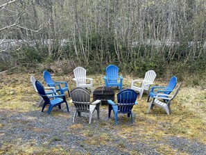 Un groupe de fauteuils Adirondack disposés autour d’un foyer central, dans un cadre extérieur.