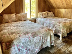 Ein gemütliches Schlafzimmer im Dachgeschoss mit zwei Betten, Holzwänden und einem großen Fenster.