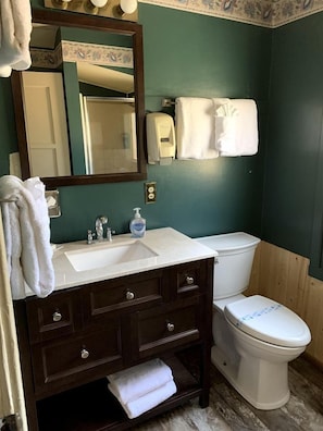 Ein Badezimmer mit dunklem Holzschrank, weißem Waschbecken, Spiegel, Toilette und Handtuchhalter.