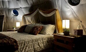 Une pièce aménagée avec une tente, un lit, des lampes de chevet et une petite table sur laquelle est posée une plante.