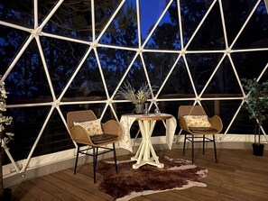A room with a large window, two wicker chairs, a small round table, and a potted plant. - Stunning Secluded Dome with Gorgeous Forest Sights in Hermosa, South Dakota (Hermosa)
