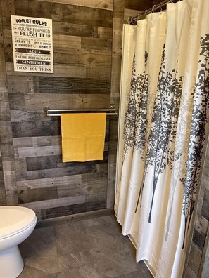 A bathroom with a wooden wall, a toilet, a towel rack with a yellow towel, and a shower curtain with a floral pattern.