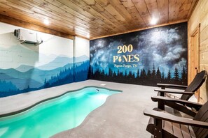 Ein Poolbereich mit Wandgemälde, Holzbalkendecke und Adirondack-Stühlen.