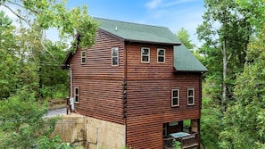 Eine mehrstöckige Blockhütte mit Balkon und Whirlpool, umgeben von dichtem Wald.