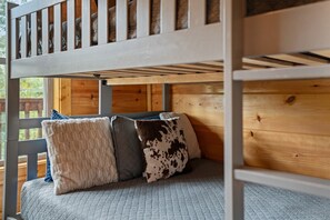 Ein Etagenbett mit Holz Kopfteil, einer grauen gesteppten Matratze und drei Kissen mit verschiedenen Mustern.