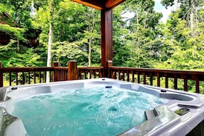 Ein Whirlpool auf einer Terrasses mit Holzgeländer, umgeben von üppigen, grünen Bäumen.