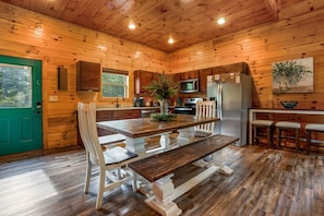 Ein Holzblockhaus-Interieur mit Esstisch, Stühlen, einer Küchenzeile und einer grünen Tür.