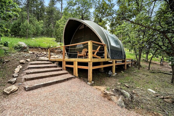 Une cabane en forme de d ôme, dotée d’une terrasse en bois et d’une chaise, entourée d’une forêt.