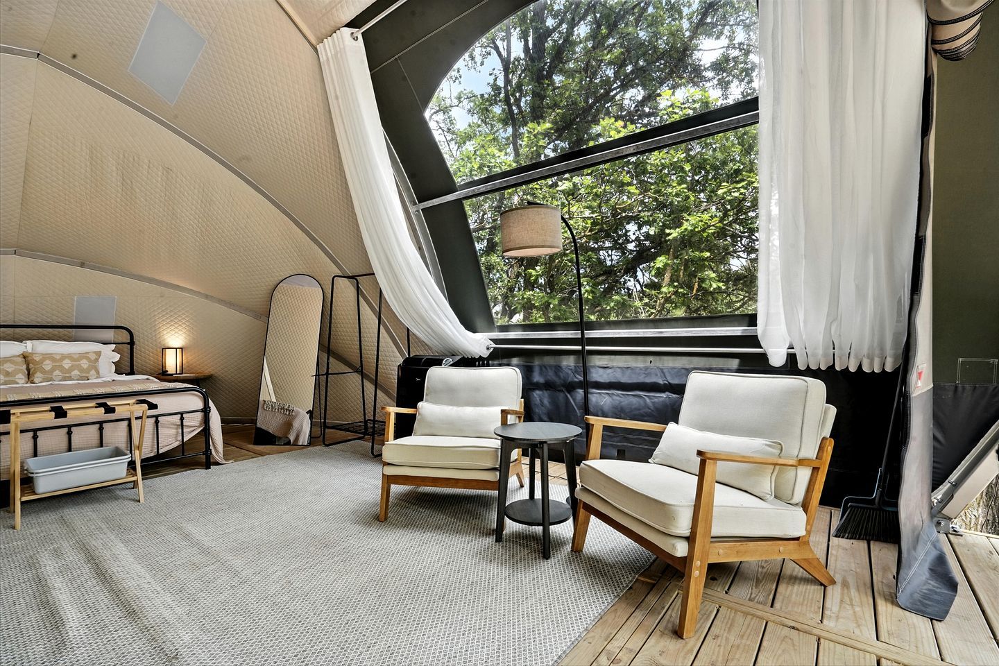 Un hébergement sous tente comprenant un lit, deux chaises, une petite table et une lampe.