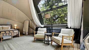 Un hébergement sous tente comprenant un lit, deux chaises, une petite table et une lampe.