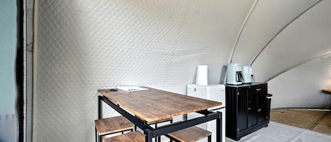 A tented room with a wooden table and benches, a coffee machine, and a cabinet.