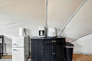 Una kitchenette compacta equipada con refrigerador, cafetera y basurero.