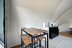 Une pièce aménagée avec une tente, une table et des bancs en bois, une machine à café et un meuble.