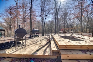 Une terrasse en bois avec un barbecue et une table de pique-nique, le tout entouré d’arbres.