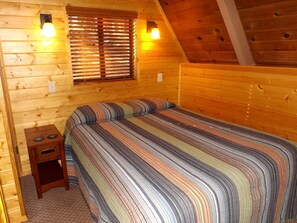 Ein Schlafzimmer einer Holzhütte mit einem Bett, einem Nachttisch und zwei Wandleuchten.