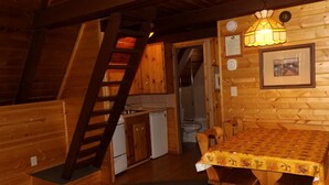 Interior de una cabaña de madera con cocina, comedor y escalera.