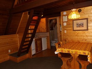 Ein Holzblockhaus mit Küche, Essbereich und Treppe.