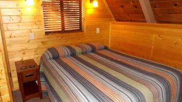 A wooden cabin bedroom with a bed, a nightstand, and two wall-mounted lights.