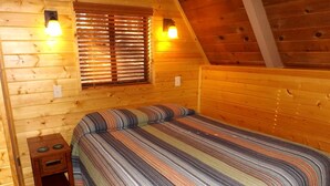 Un dormitorio de cabaña de madera con una cama, una mesita de noche y dos luces fijadas a la pared.