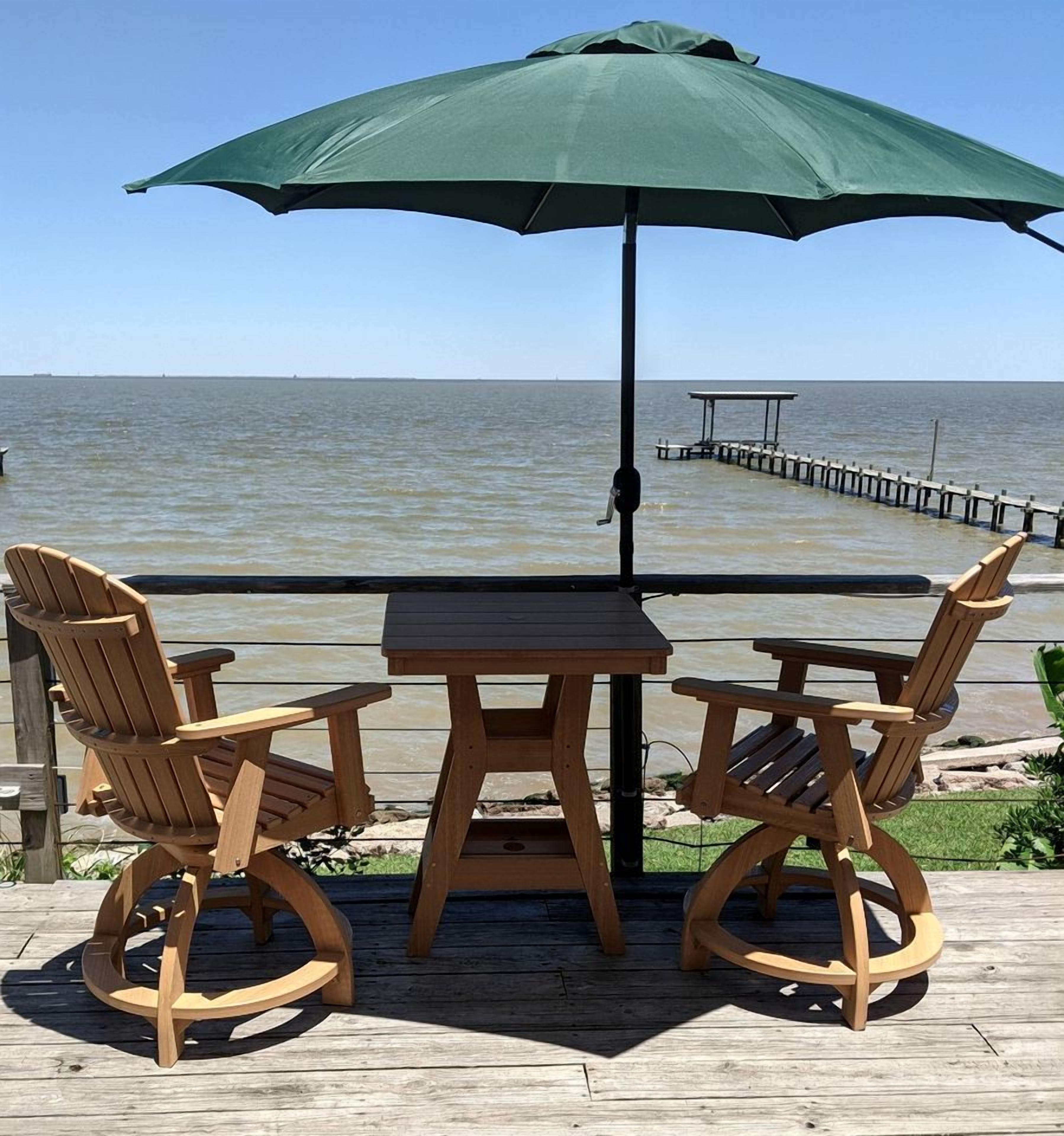 A wooden deck with two Adirondack chairs and a table under a green umbrella, overlooking a body of water and a pier.