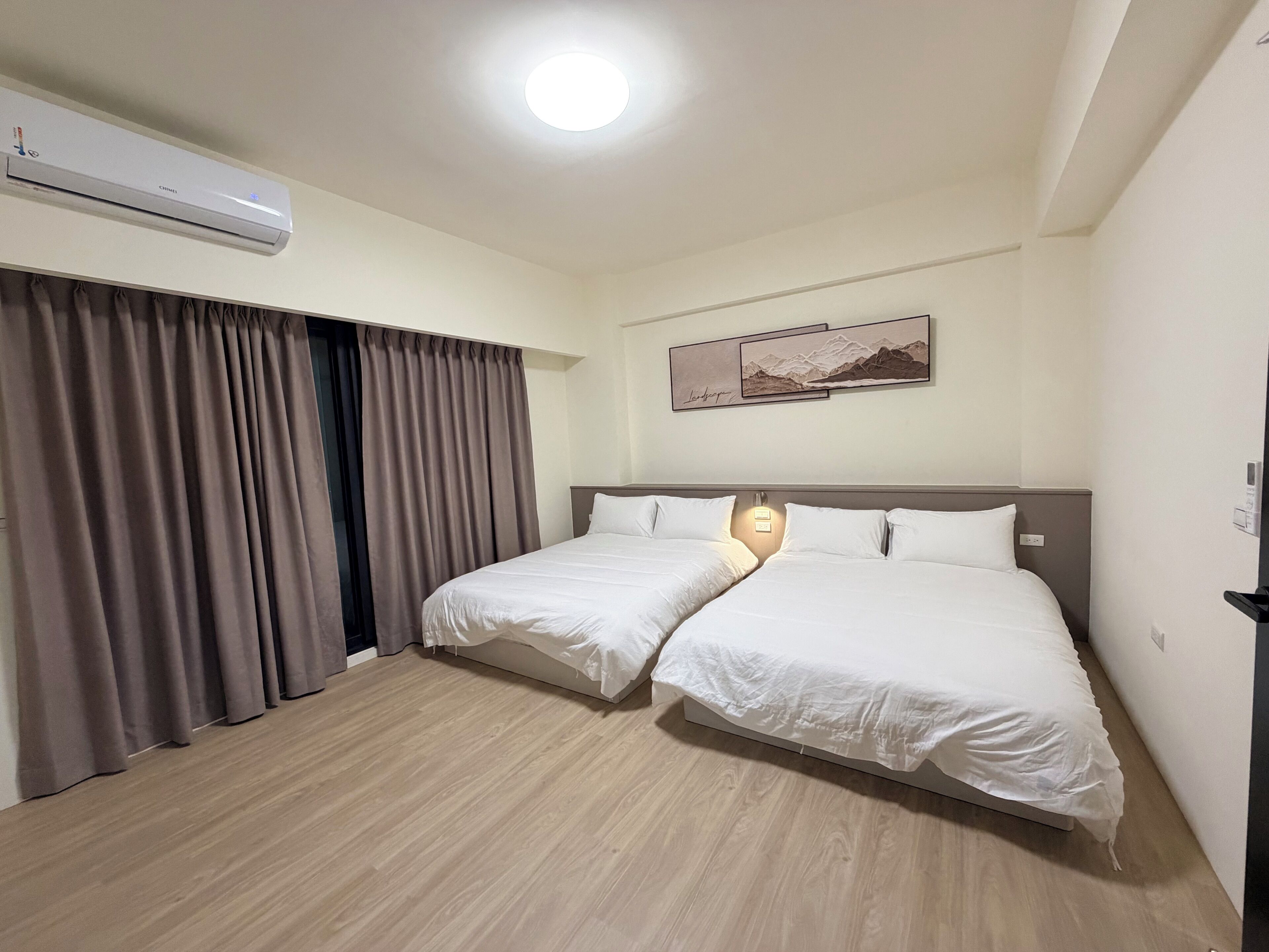Une chambre d’hôtel avec deux lits, un ventilateur de plafond, un appareil de climatisation, un tableau au mur et un luminaire au-dessus des lits.