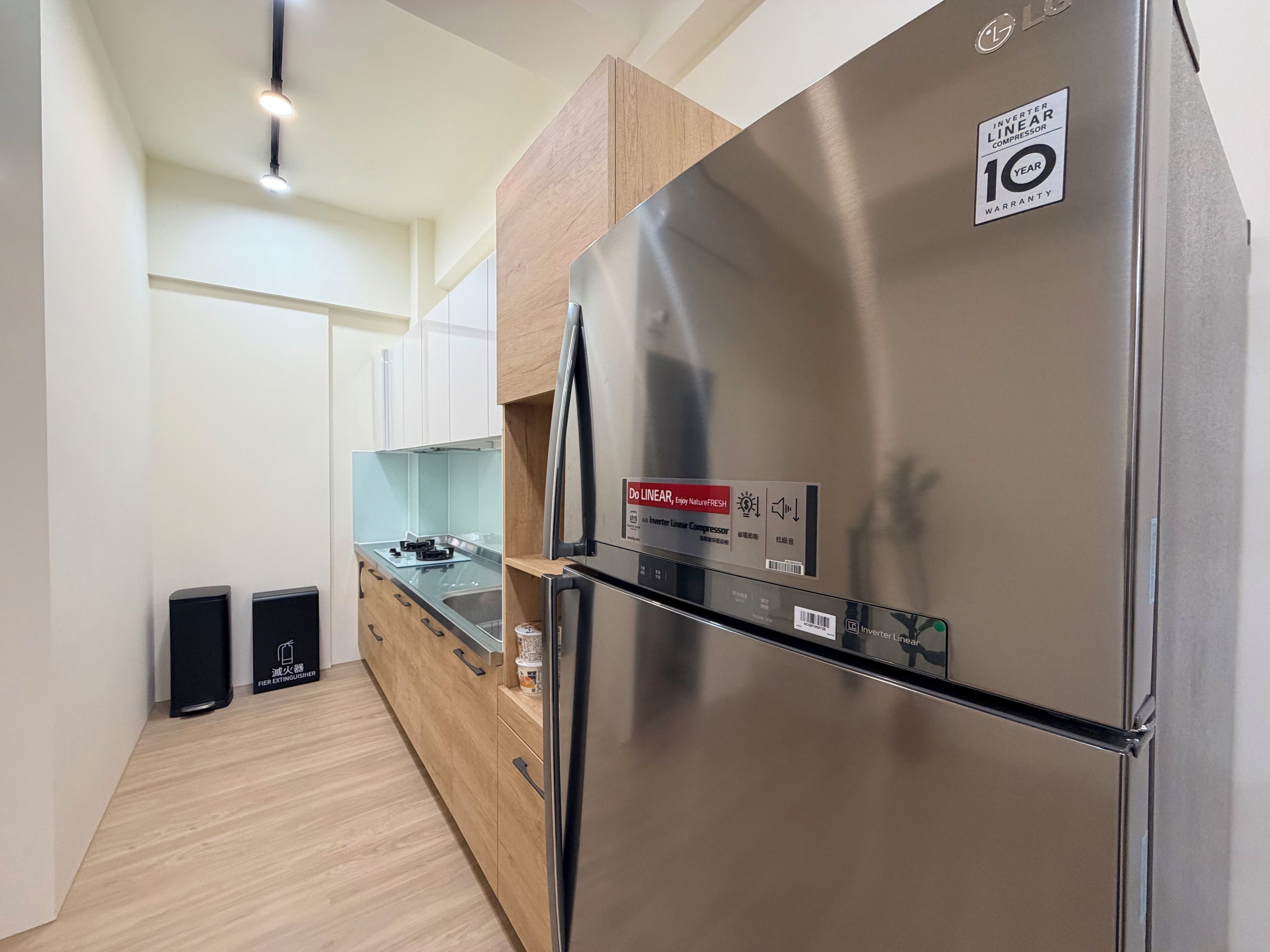 A modern kitchen with a stainless steel refrigerator, wooden cabinets, a built-in oven, and a sink.