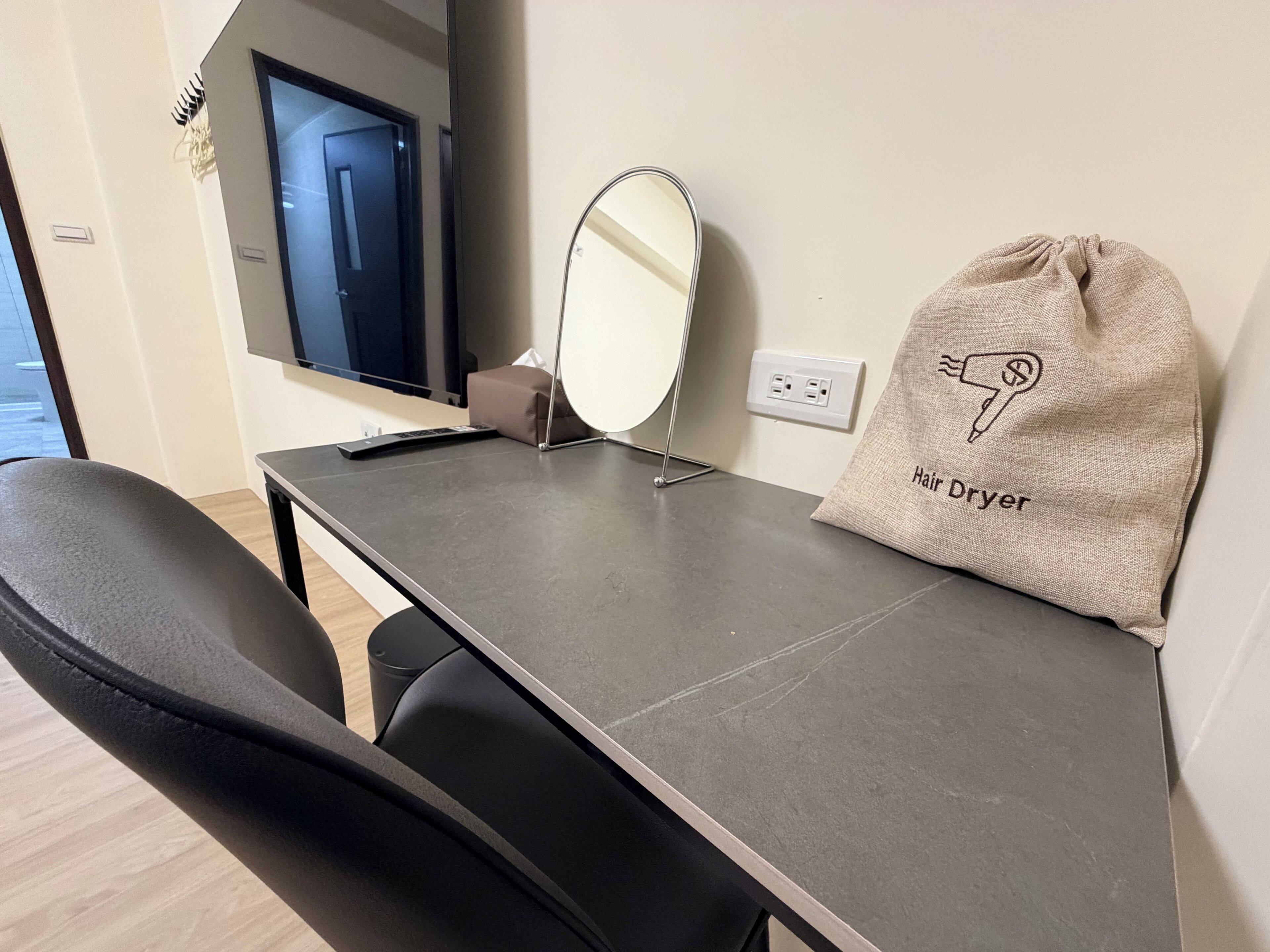 Una habitación de hotel moderna con escritorio, espejo, neceser para secador y televisor.