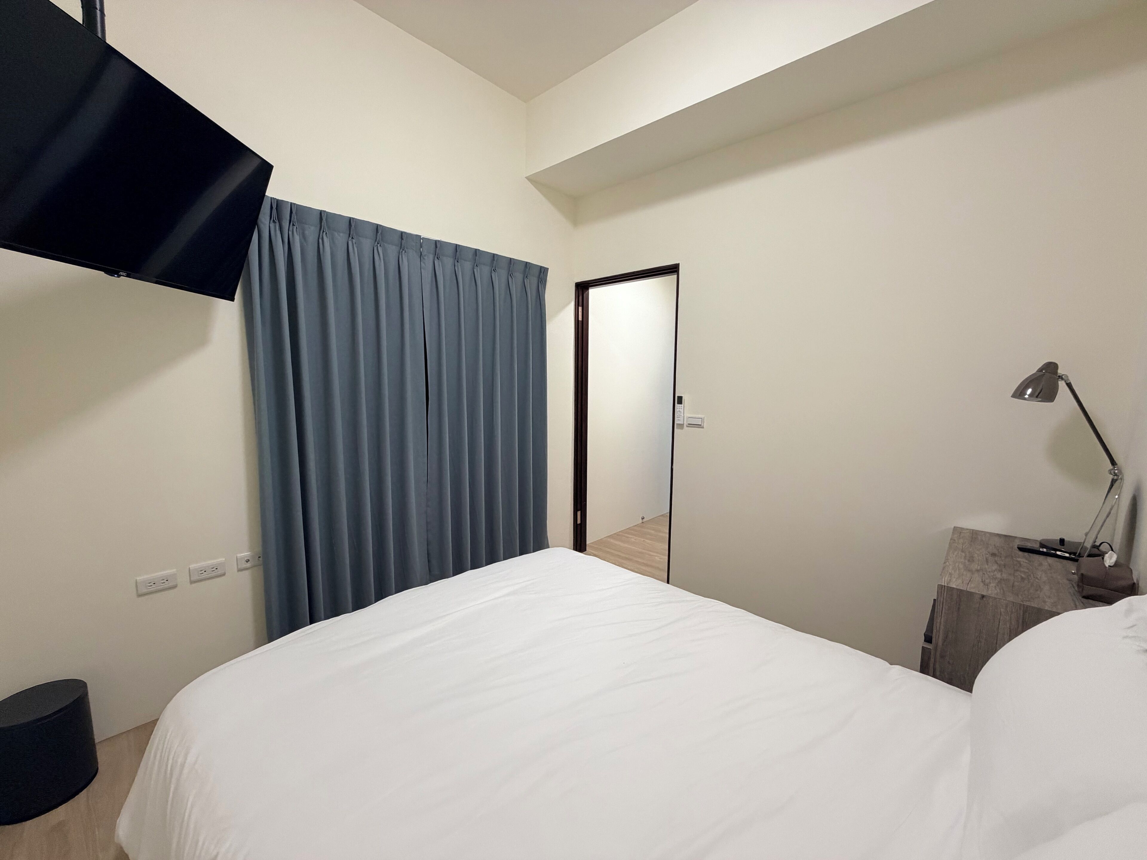 Et hotelværelse med seng, skrivebord med lampe, fjernsyn og dør.