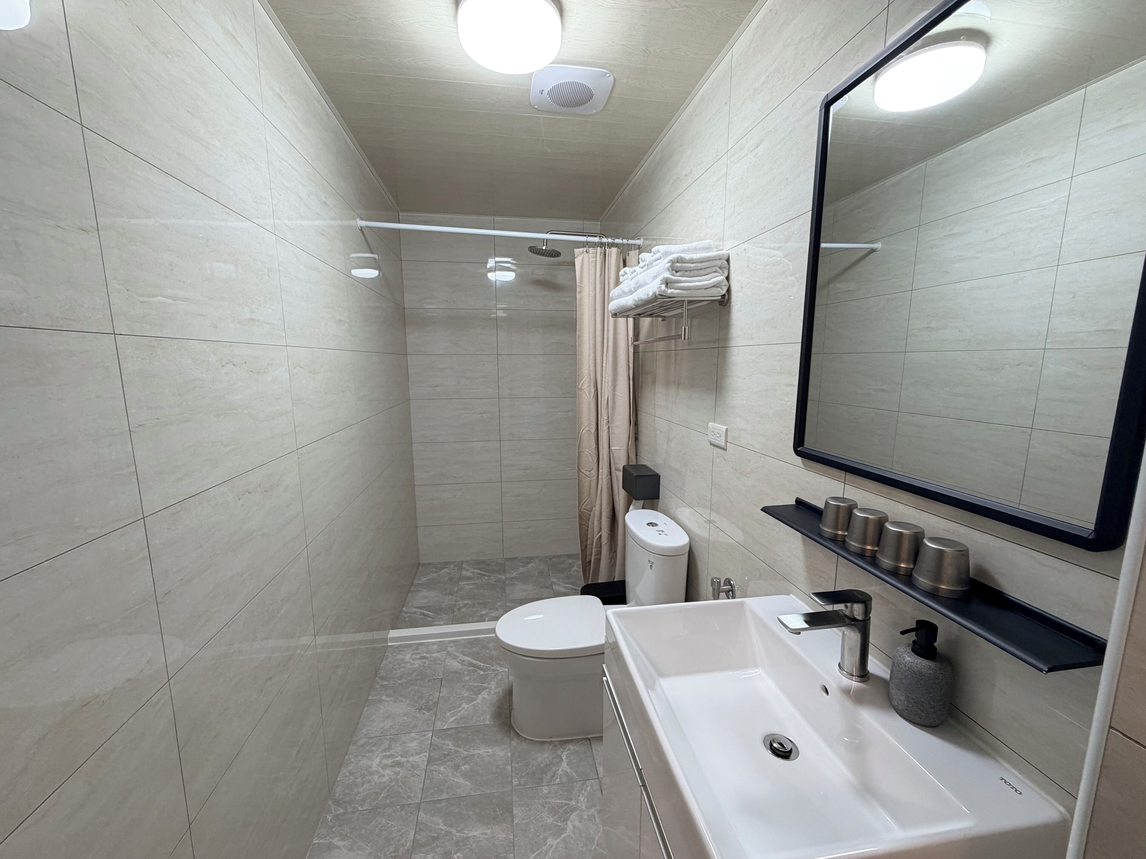 A modern bathroom with a shower, toilet, and sink, featuring a large mirror and tiled walls.