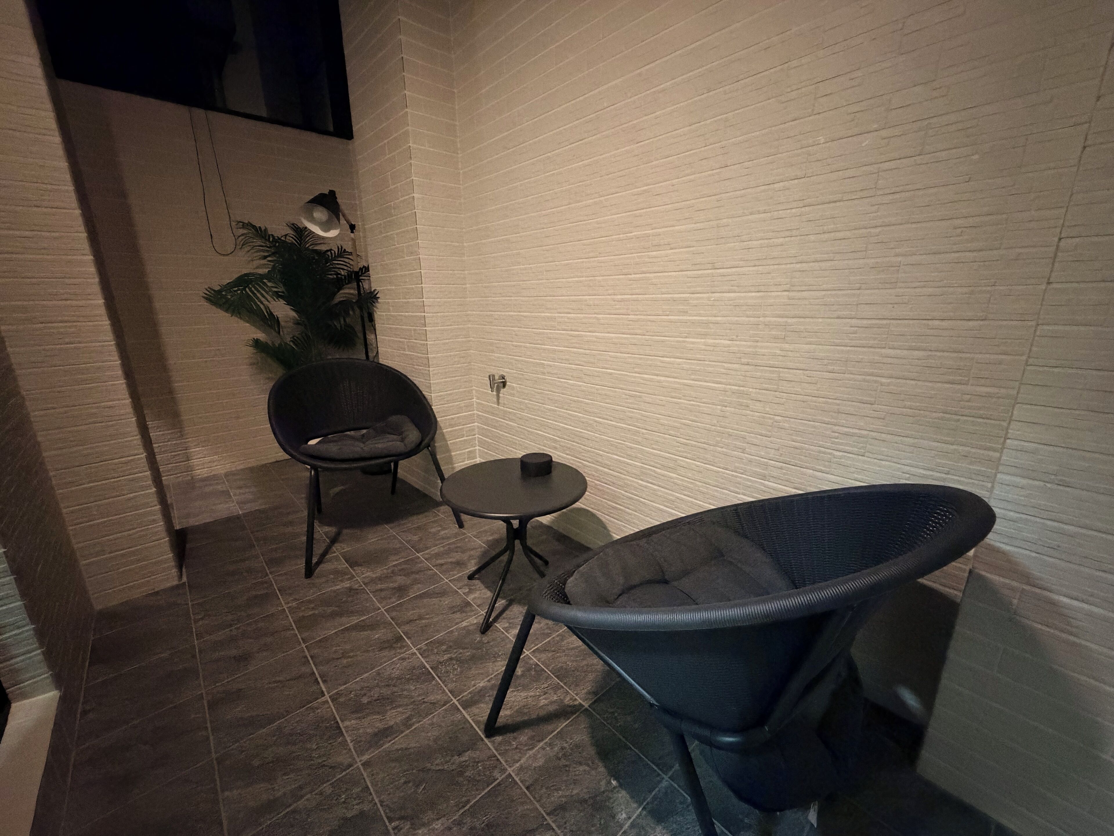 A small, enclosed space with a tiled floor, two chairs, a small table, and a potted plant.