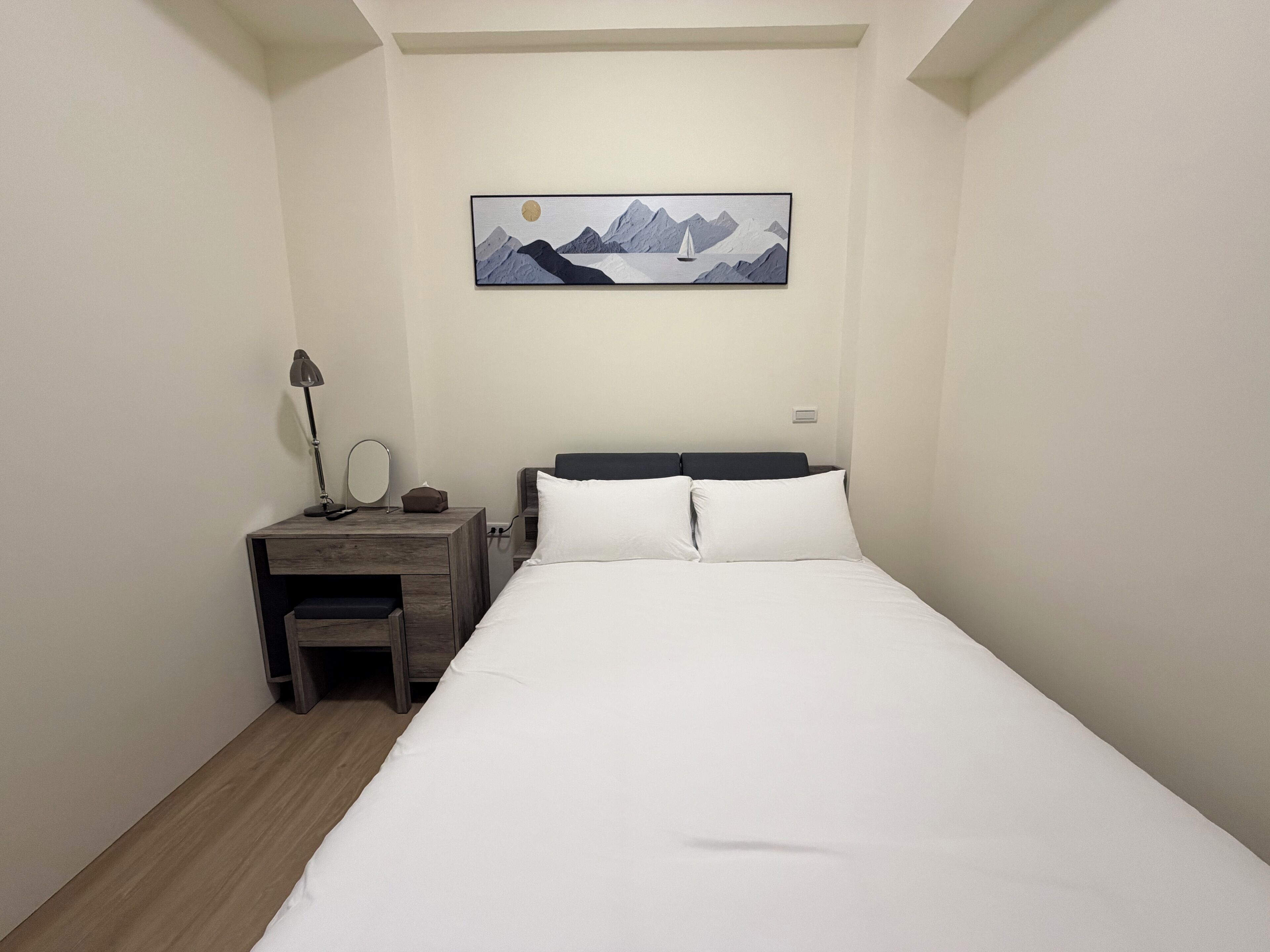 Un dormitorio con cama, escritorio, silla, lámpara, espejo y un cuadro en la pared.