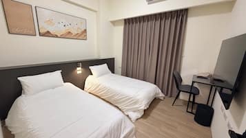 A hotel room with two beds, a desk with a chair, an air conditioner, and two wall-mounted artworks.