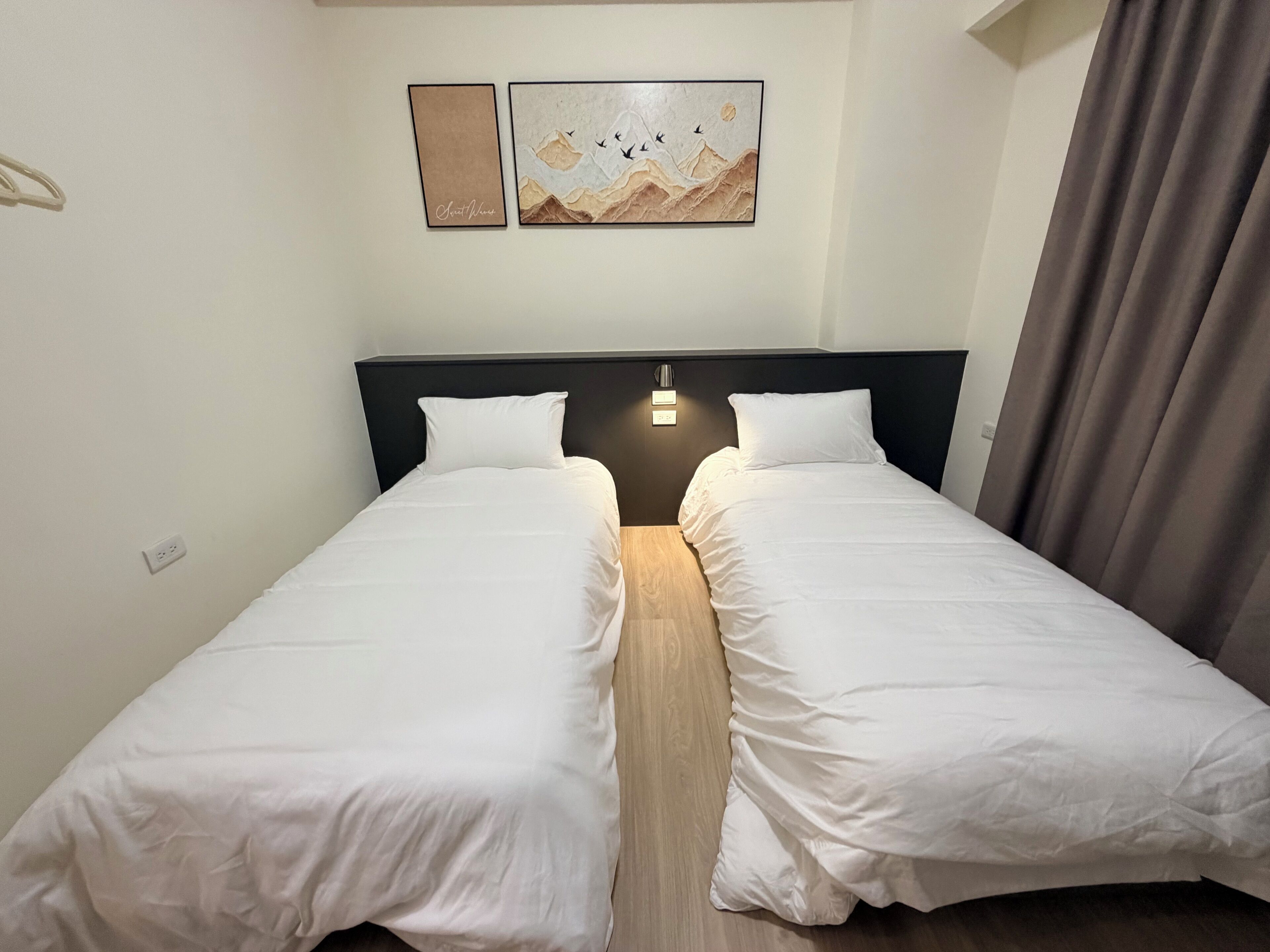 Un lit double avec une literie blanche, une tête de lit en bois et deux interrupteurs d’éclairage fixés au mur.
