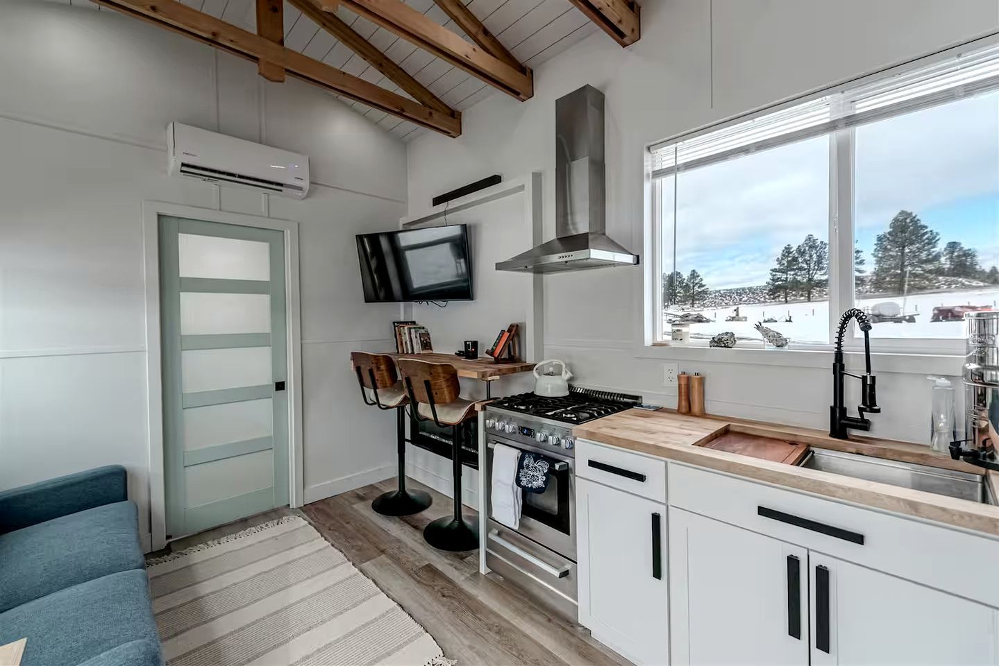 Una cocina moderna con armarios blancos, una estufa empotrada, un ventanal con vistas y un televisor montado sobre la encimera.
