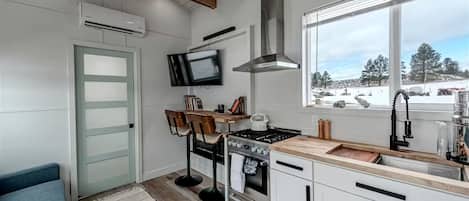 Una cocina moderna con armarios blancos, una estufa empotrada, un ventanal con vistas y un televisor montado sobre la encimera.
