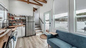 Una cocina moderna con un refrigerador de acero inoxidable, vigas de madera, horno empotrado y ventana con vistas a un paisaje nevado.