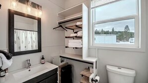 Un baño moderno con un espejo grande, lavamanos blanco, toallero y una ventana con vistas a árboles.
